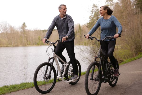 Mann und Frau fahren nebeneinander Stepper-Fahrrad auf einem Weg an einem See.